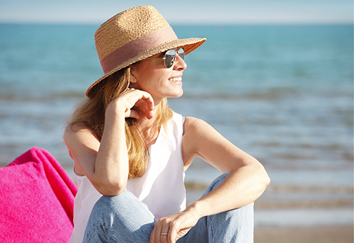 Portait of happy mature woman wearing straw hat and sunglasses while at the beach on a sunny day.